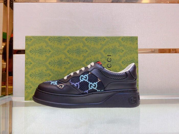 Sneakers Gucci nere con monogramma blu, su elegante packaging verde di lusso.