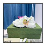 Sneakers bianche con graphic di leone, su scatola verde elegante, sfondo con tende blu soft.