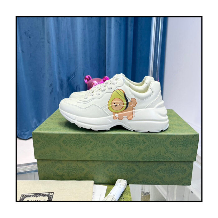 Sneakers bianche con graphic di leone, su scatola verde elegante, sfondo con tende blu soft.