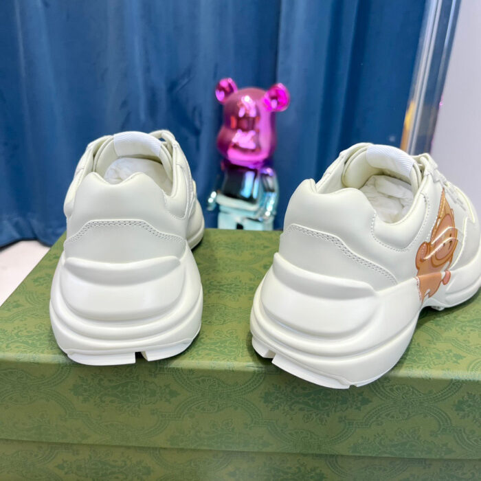 Sneakers moderne con dettagli lucidi e orsetto rosa giocoso sullo sfondo, stile streetwear.
