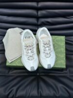 Sneakers bianche di lusso con logo, dettaglio metallici e accessori eleganti su sfondo nero.