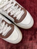 Sneakers bianche e marroni eleganti su sfondo rosso, stile moderno e comfort sportivo.