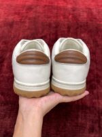 Sneakers bianche con dettagli marroni su fondo rosso, stile moderno e versatile.