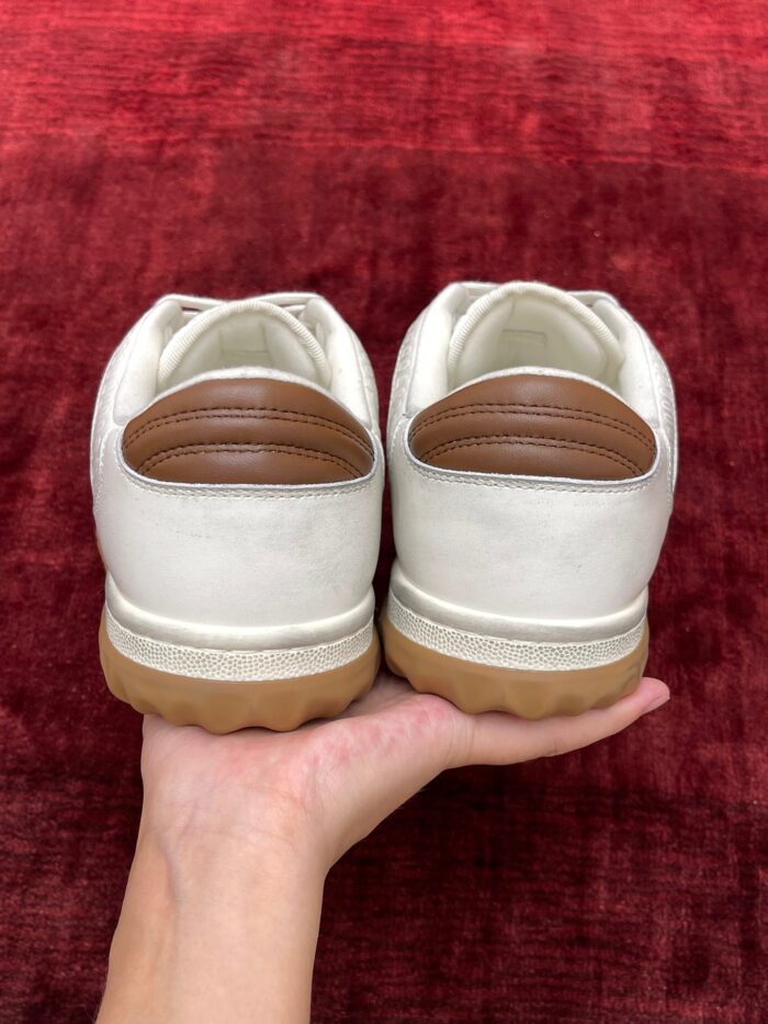 Sneakers bianche con dettagli marroni su fondo rosso, stile moderno e versatile.