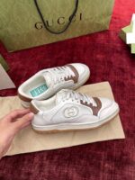 Sneakers Gucci di lusso bianche con dettagli in pelle marrone su sfondo burgundy elegante.