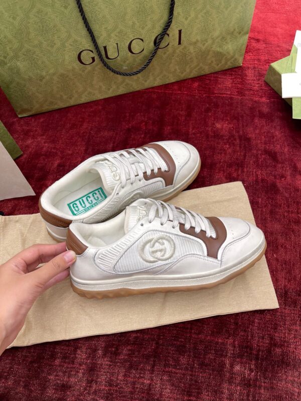 Sneakers Gucci di lusso bianche con dettagli in pelle marrone su sfondo burgundy elegante.