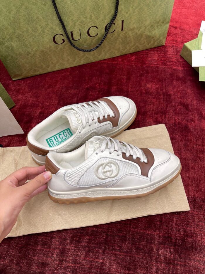 Sneakers Gucci di lusso bianche con dettagli in pelle marrone su sfondo burgundy elegante.
