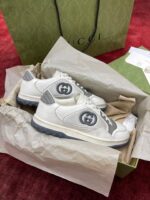 Sneakers Gucci bianche e grigie in confezione elegante su sfondo rosso.
