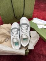 Sneakers Gucci bianche e grigie, confezione di lusso su tappeto rosso elegante.
