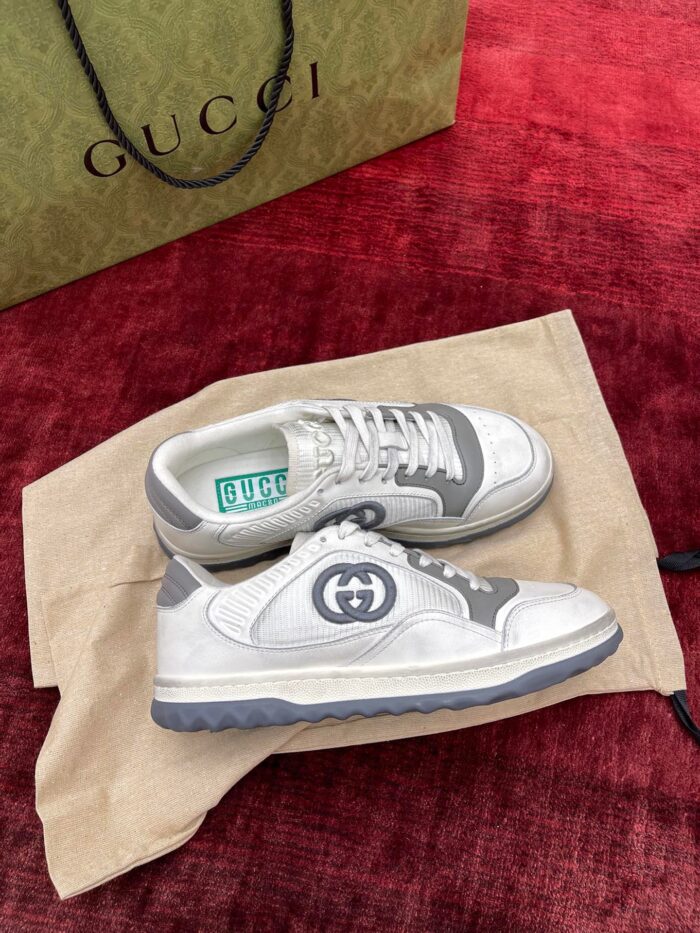 Scarpe Gucci eleganti su superficie rossa, con dust bag e shopping bag verde in evidenza.