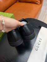 Scarpe Gucci nere in pelle con dust bag di lusso su tavolo in controluce elegante.
