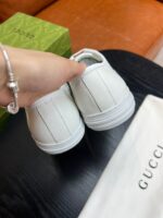 Sneaker Gucci bianca di lusso con bracciale elegante, sullo sfondo divano arancione e scatola verde.