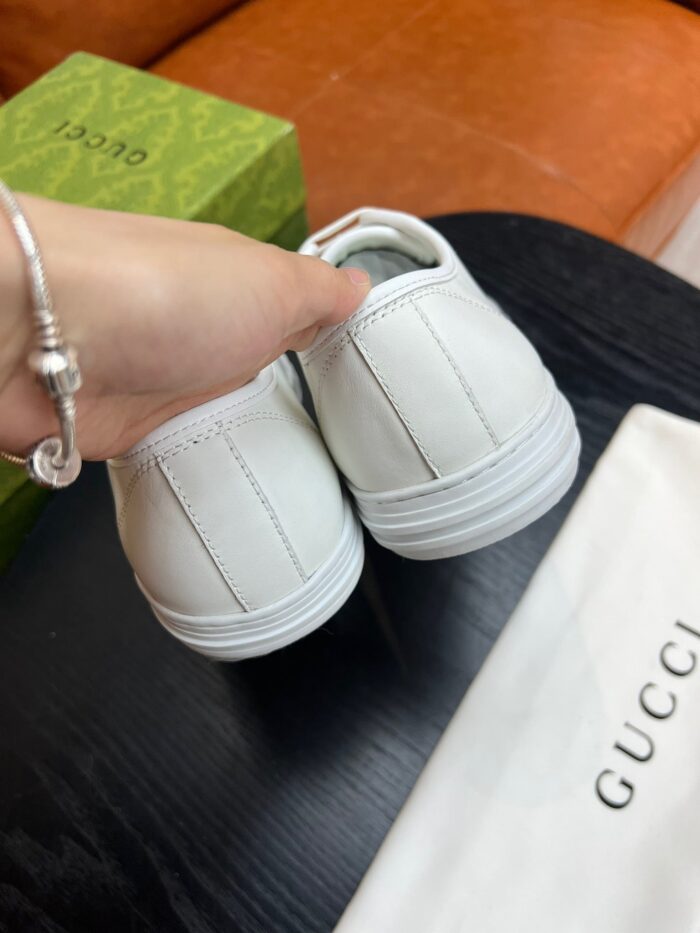 Sneaker Gucci bianca di lusso con bracciale elegante, sullo sfondo divano arancione e scatola verde.