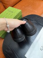 Scarpe Gucci nere in pelle con confezione di lusso su tavolo in legno lucido.