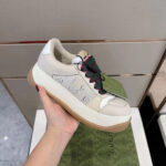 Sneaker Gucci beige con lacci verde rosso, stile casual e sofisticato, su suola in legno chiaro.