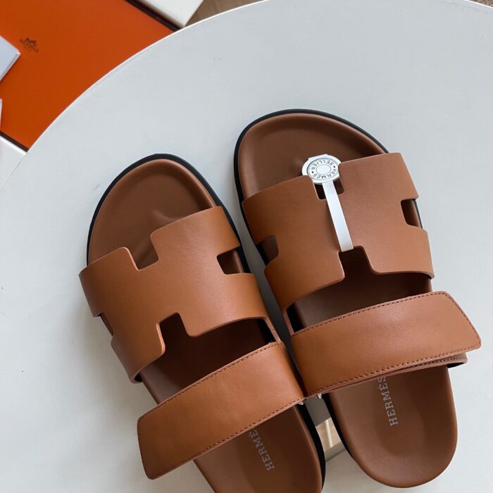 Sandali eleganti in pelle marrone con cinturini a taglio, dettaglio metallico, su tavolo rotondo.