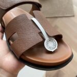 Sandalo Hermès in pelle marrone con logo bianco, stile luxury elegante e comodo per lestate.