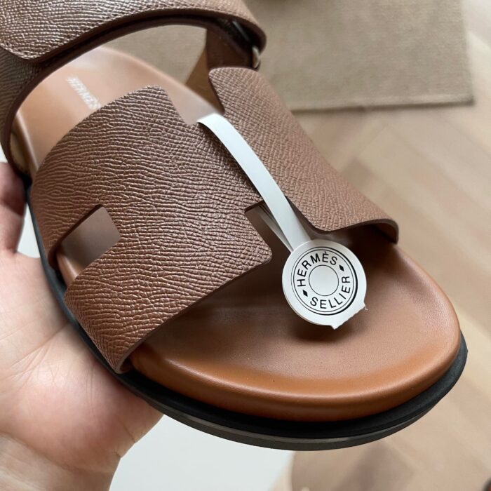 Sandalo Hermès in pelle marrone con logo bianco, stile luxury elegante e comodo per lestate.