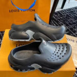 Scarpe moderne Louis Vuitton nere con dettagli grigi, su scatola arancione e tappeto nero elegante.