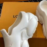 Scarpe futuristiche bianche con design organico su scatola arancione, elegante e versatile.