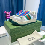 Sneakers di lusso con lacci blu, dettagli colorati e packaging elegante su sfondo blu e rosa.