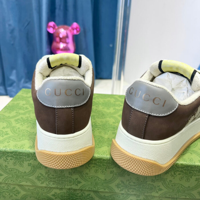Sneakers Gucci in pelle marrone con logo ricamato, su elegante scatola decorata, con teddy rosa sullo sfondo.