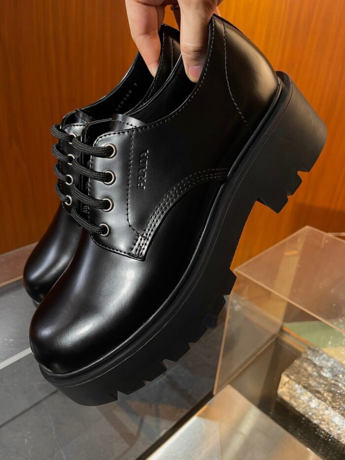 Scarpe Oxford nere con suola spessa, stile elegante e design moderno su superficie in legno.