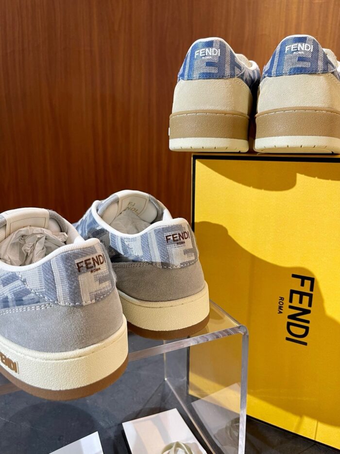 Sneakers di lusso Fendi con dettagli in tessuto e suede su supporto trasparente, scatola gialla elegante.