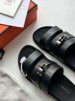 Sandali neri di lusso con cinturini moderni, dettagli metallici e elegante packaging arancione.