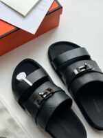 Sandali neri di lusso con dettagli metallici, su superficie chiara con scatola elegante e note.