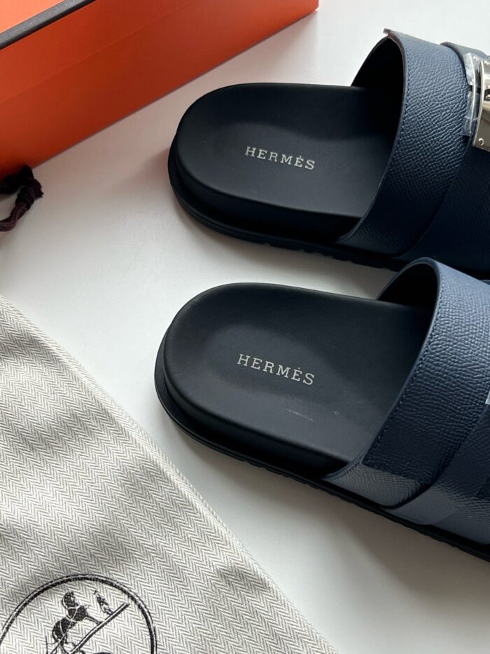 Sandali Hermès navy stile modern con logo, packaging iconico e accessori eleganti.