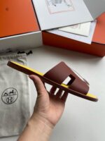 Sandali di lusso in pelle marrone con suola gialla vivace e dettagli moderni.