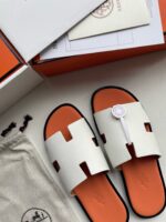 Sandali bianchi eleganti con dettagli arancioni, packaging di lusso e accessori coordinati.