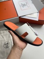 Sandalo minimalista di lusso con suola arancione e dettagli eleganti, in confezione di marca esclusiva.