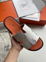Sandalo minimalista bianco con suola arancione, packaging elegante, stile moderno e comfort premium.