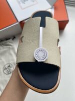 Sandalo di lusso con logo, fascia beige traforata, su sfondo arancione vibrante e fondo blu navy.