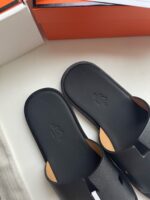 Sandali neri eleganti con logo minimalista e design moderno su superficie bianca.
