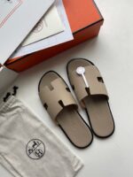 Sandali beige di lusso con strap a forma di H, confezionati in box arancione elegante.