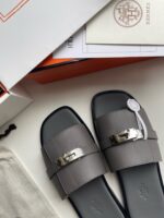 Sandali di lusso grigi con fibbia argento, packaging elegante e stile sofisticato in mostra.