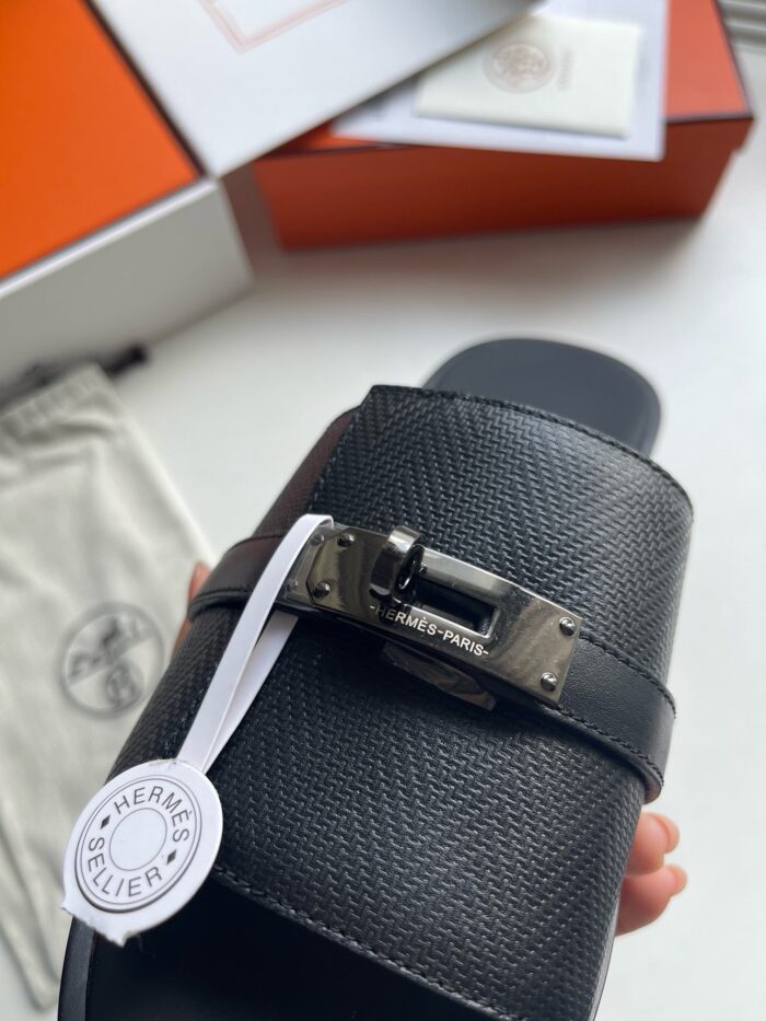Sandalo slip-on in pelle nera con fibbia metallica, brand di lusso su sfondo bianco e scatola arancione.