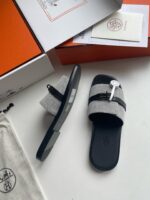 Sandali di lusso con dettagli moderni, strap nero e packaging esclusivo su sfondo bianco.