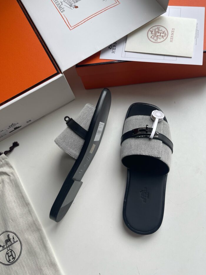 Sandali di lusso con dettagli moderni, strap nero e packaging esclusivo su sfondo bianco.