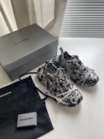 Sneakers Balenciaga di lusso con scatola e dust bag su superficie bianca elegante.