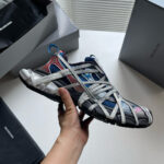 Sneaker innovativa di design premium con fasce elastiche, colori grigi, blu e rossi, stile moderno.