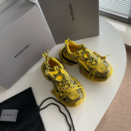 Scarpe sportive gialle Balenciaga su tavolo bianco con scatole e borsa elegante.