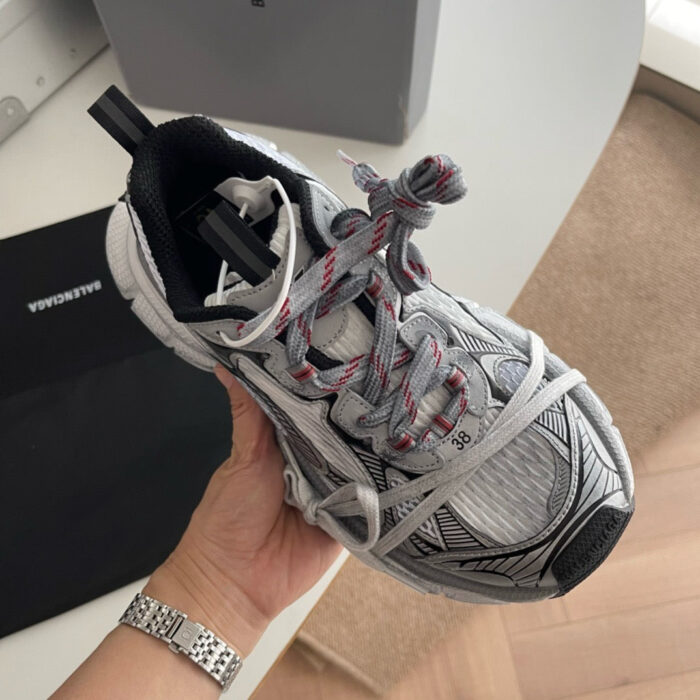 Sneaker moderna grigia con lacci rossi, design sportivo e stile minimalista in interno elegante.