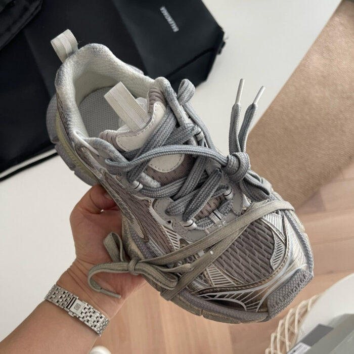 Sneaker sportiva moderna con lacci intrecciati, in tonalità grigia, portata a mano in ambiente casual.