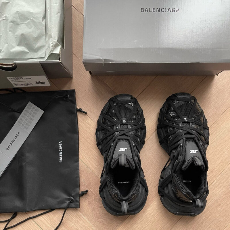 Sneakers Balenciaga nere con confezione di lusso e sacca su pavimento di legno caldo.