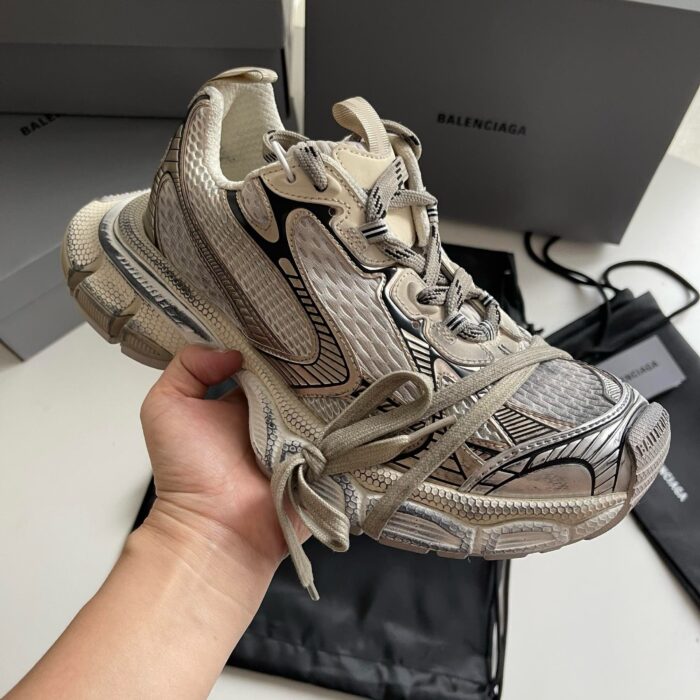 Sneaker di lusso streetwear con dettagli innovativi e design elegante in tonalità beige e grigia.