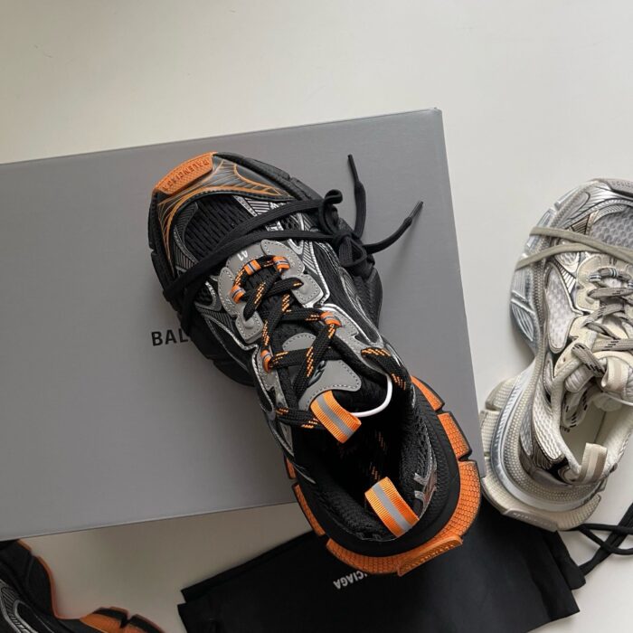 Sneakers moderne in stile urban con dettagli arancioni e confezione elegante su sfondo neutro.